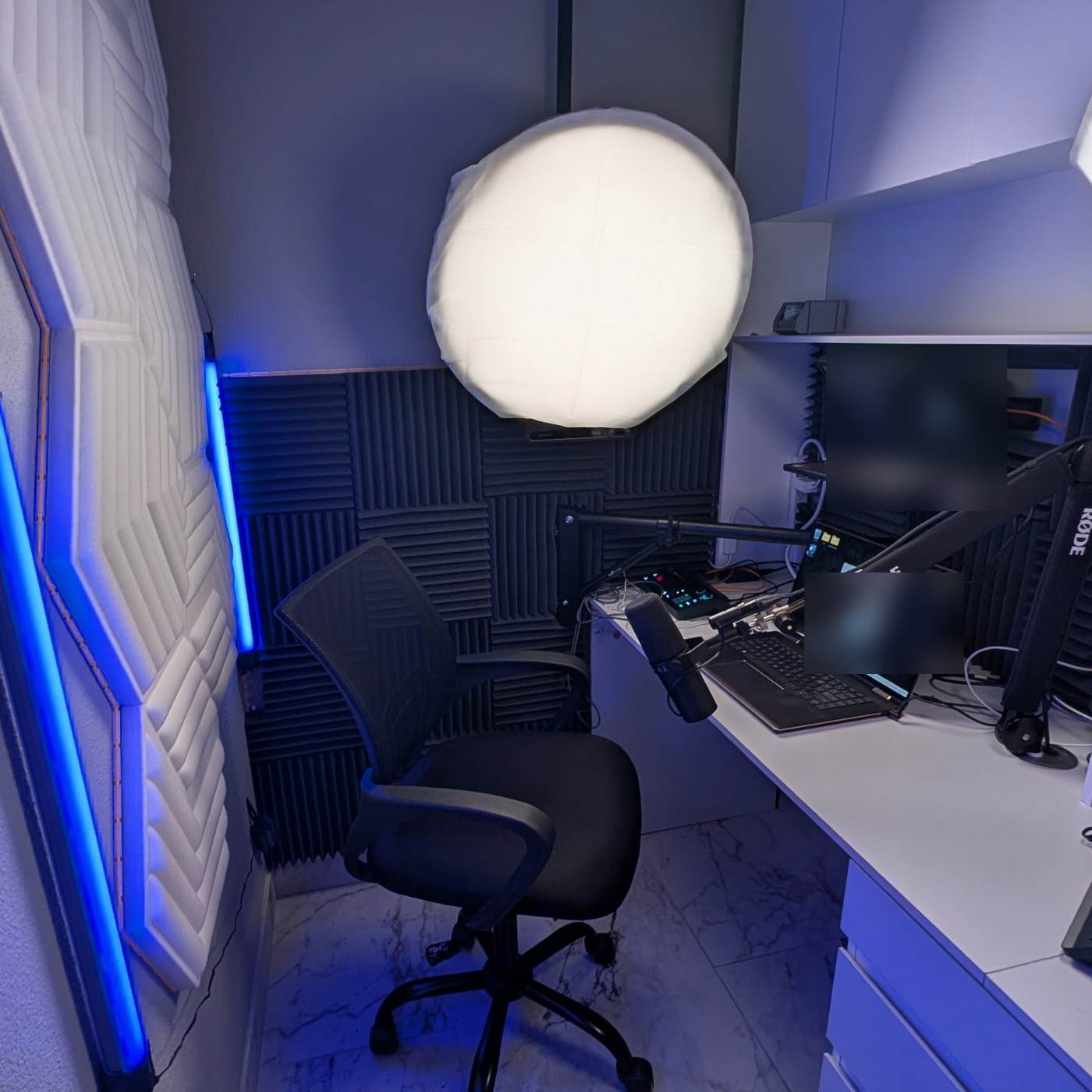 The same corner finished as a recording studio with acoustic panels, a key light, a teleprompter rig, and a microphone